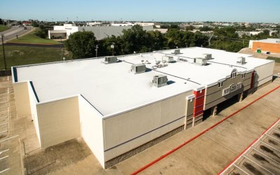 Aerial view of a flat-roofed commercial building with rooftop HVAC units, surrounded by an empty parking lot and nearby road.