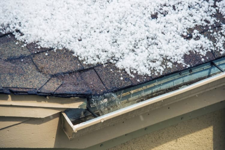 Hailstones covering the roof and filling the gutter of a house show why expert help from Shane Fisk Roofing is essential.